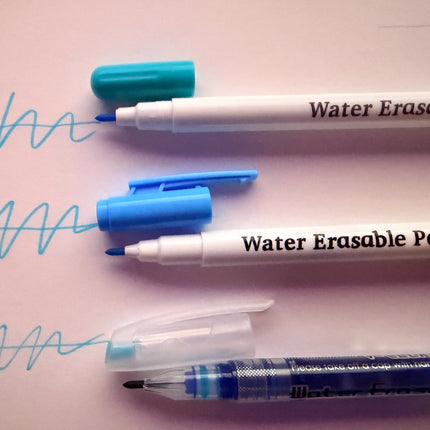 Water erasable pens with blue and white caps on a light pink background.
